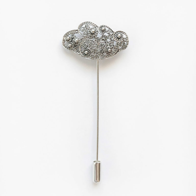 Una original joya en forma de prendedor de aguja largo con una nube de diseño en filigrana con espirales y pequeñas bolas ornamentales